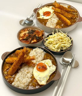 Two curry rice plates with fried shrimp and eggs alongside kimchi and cabbage side dishes
