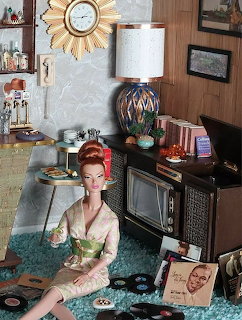 Fashion doll seated in a retro living room diorama with a television, record player, lamp, and clock