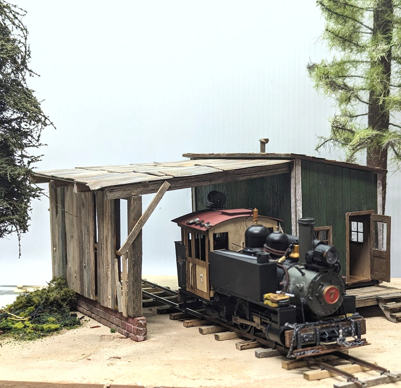 Small steam locomotive on narrow tracks beside a wooden shed outdoors