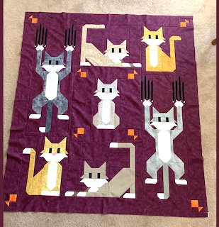 Patchwork quilt with six stylized cats on a purple background