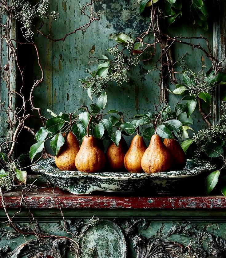 Golden pears with leaves on a mossy stone tray against a peeling green vintage wall