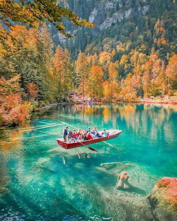 Turquoise alpine lake with a tourist boat and colorful autumn trees along rocky cliffs