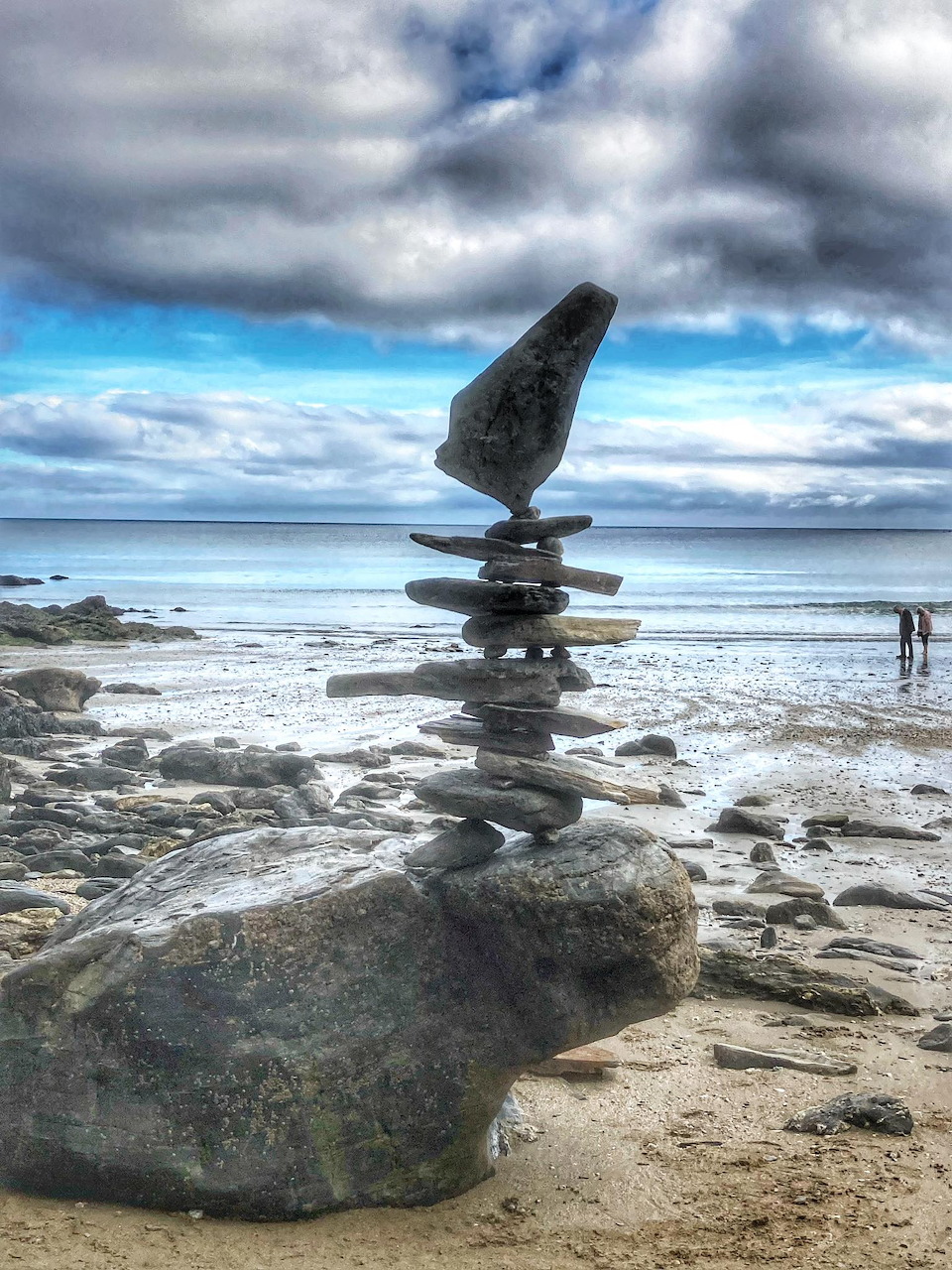 Stacked rocks balancing on beach with stormy sky and ocean horizon