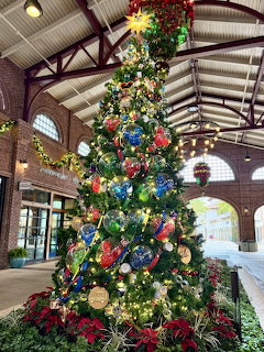 Tall Christmas tree decorated with colorful ornaments and lights in indoor pavilion with exposed beam ceiling