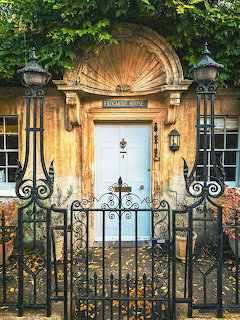 Stone building entrance with white door, iron gate, wall lanterns, and ivy frame