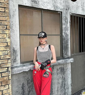 Young woman in red pants and black cap standing by a window on a weathered wall