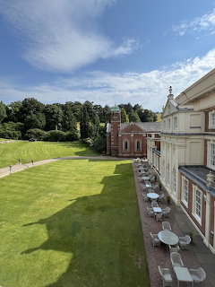 Aerial view of a grand estate with green lawn, terrace furniture, and red brick building among trees