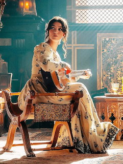 Woman in a floral vintage dress sitting indoors with a guitar beside antique furniture