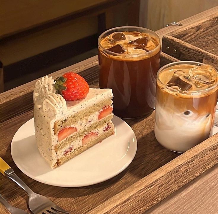 Slice of strawberry cream cake with two iced coffee drinks on a wooden tray