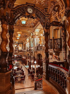 Lavish baroque café interior with gold columns, arched ceilings, chandeliers, and dining tables in Budapest