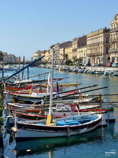 Colorful wooden fishing boats docked in a Mediterranean harbor with historic buildings in the background.