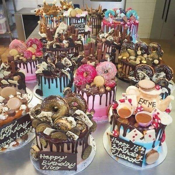 Table covered with many decorated cakes, donuts, cookies, and desserts in various colors with dripping icing