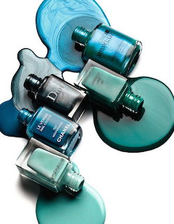 Five teal and blue nail polish bottles with spilled polish on a white background