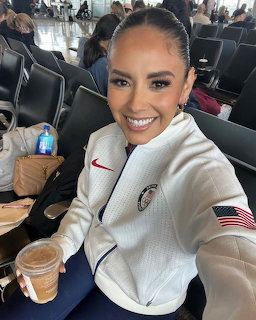 Smiling woman in a white jacket taking a selfie in an airport seating area