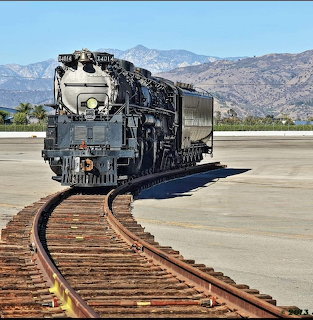 Black steam locomotive on curved train tracks with mountains in the background