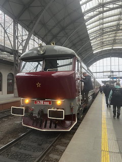 Maroon locomotive at a covered train station platform with people nearby