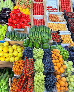 Colorful market stall with crates of fresh fruits and vegetables including grapes, tomatoes, cucumbers, and lemons