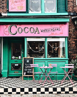 Pink and turquoise Cocoa Wonderland chocolate shop with bistro tables and checkered pavement