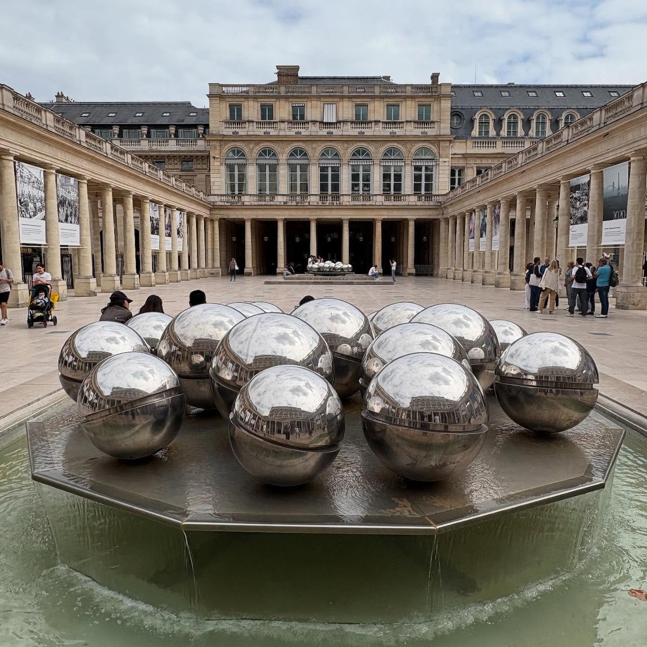 Reflective metal spheres in a fountain courtyard surrounded by classical arcades in Paris