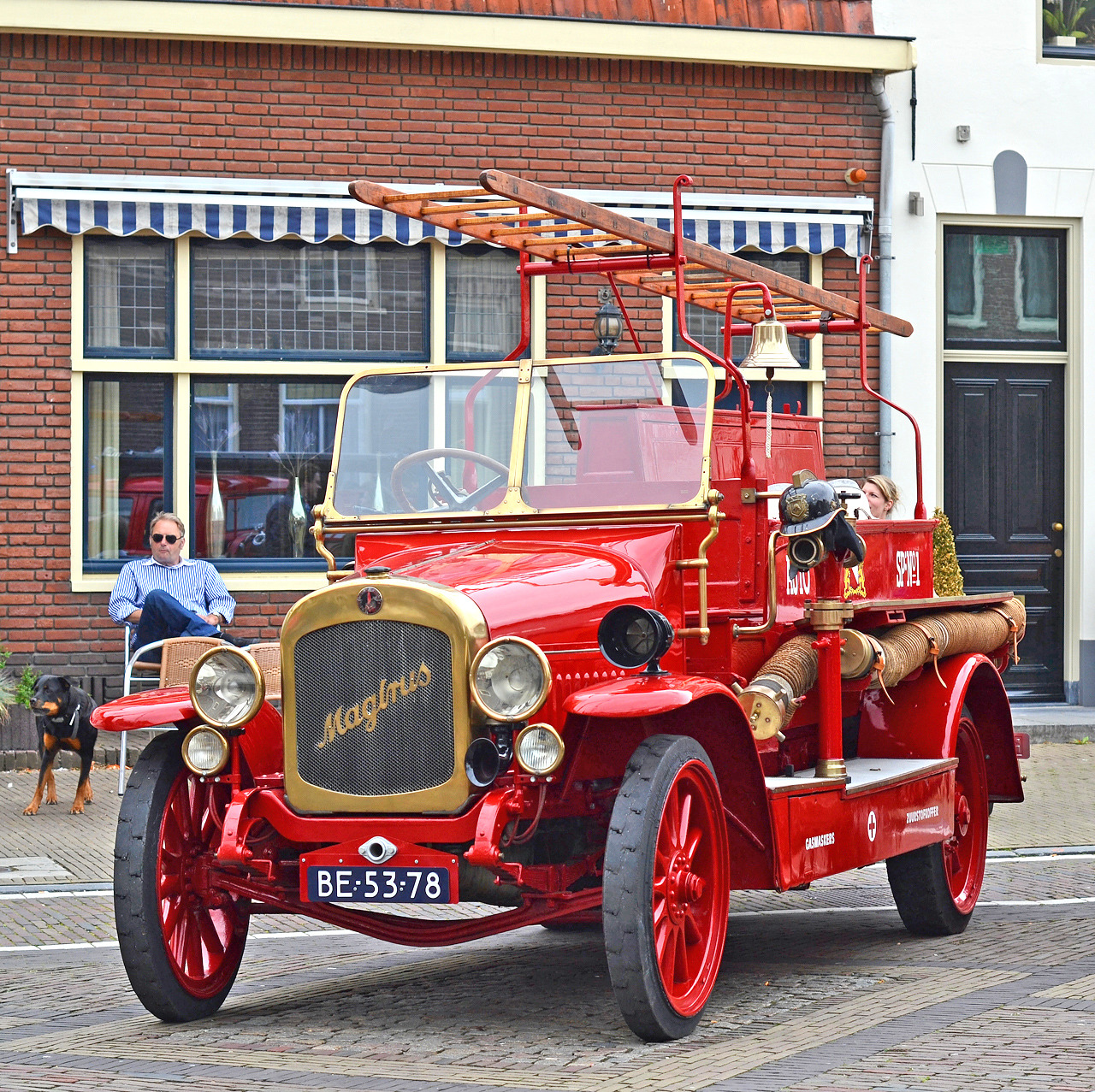 Red vintage 1959 Magirus Deutz fire truck parked on cobblestone street with brick buildings in background