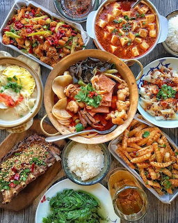 Overhead view of various Asian dishes on a wooden table including soups, seafood, rice and vegetables