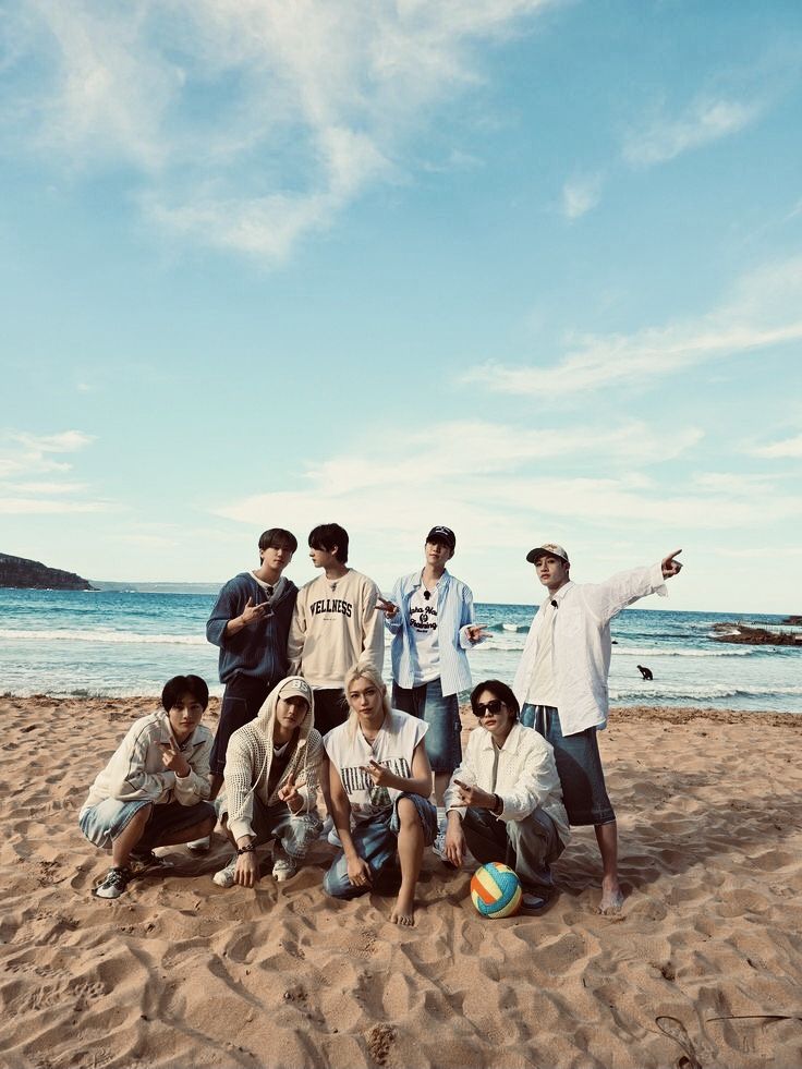 Group of young men posing on a sandy beach with ocean and blue sky behind them