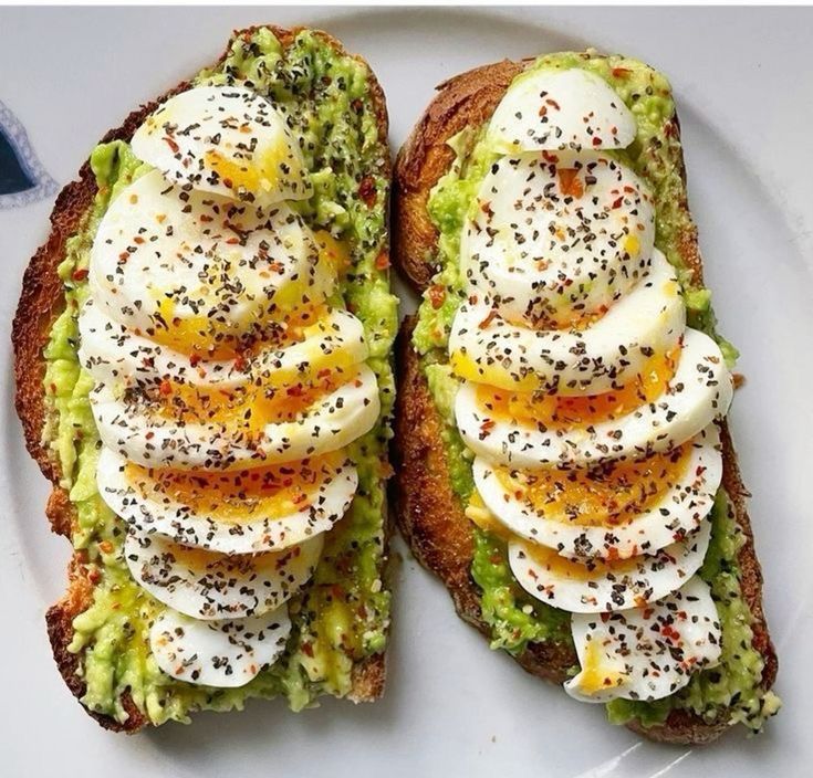 Two avocado toasts topped with sliced boiled eggs and black sesame seeds