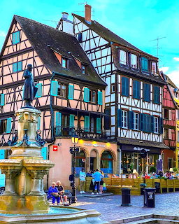 Half-timbered buildings and a stone fountain in a cobblestone square in Colmar, France