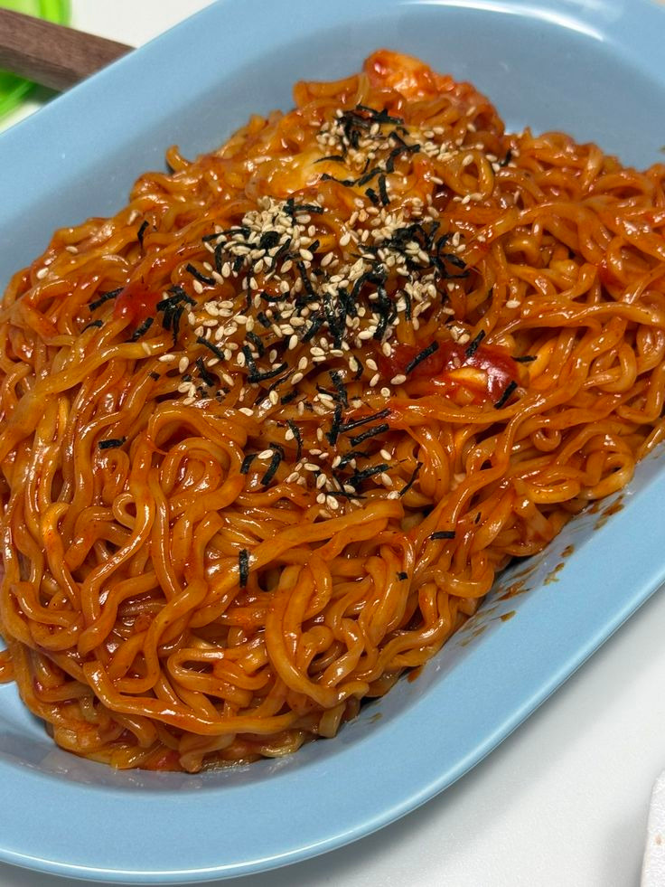 Spicy red-sauced noodles topped with sesame seeds and seaweed on a blue plate
