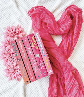 Stack of pink romance novels with a pink scarf in heart shape and pink flower on white blanket