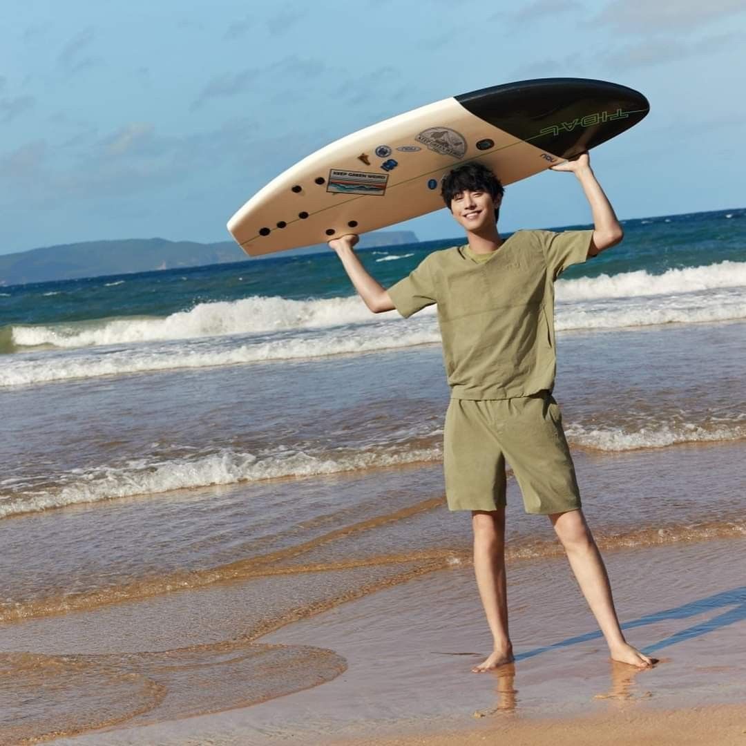 Man standing on a sandy beach holding a surfboard over his head by the ocean