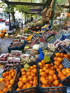 Outdoor market stall filled with oranges, berries, vegetables, and hanging onions on a cobbled street