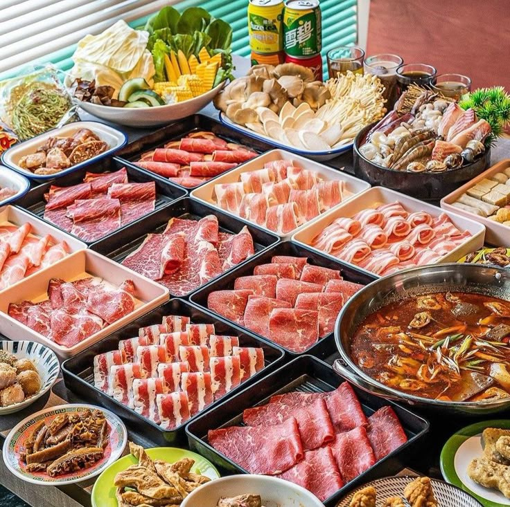 Korean food spread with sliced beef, hot pot, vegetables, mushrooms, and side dishes on a table
