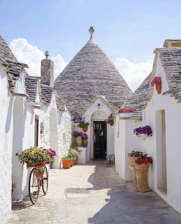 White trulli houses with grey conical roofs along a narrow street with flowers and a bicycle