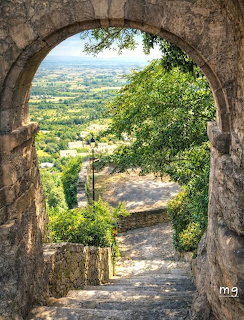 Stone arch frames descending path overlooking green valley and countryside