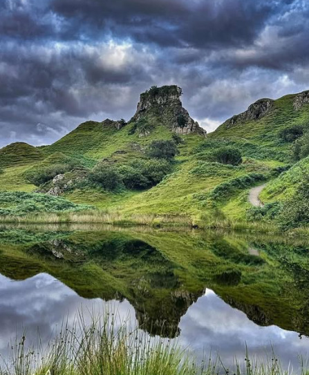 Rocky green hills reflected in a calm loch under dark cloudy skies