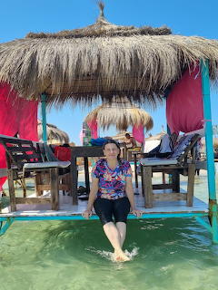 Woman sitting on lounge chair under thatched beach umbrella with colorful towels at Coucou Beach Tunisia