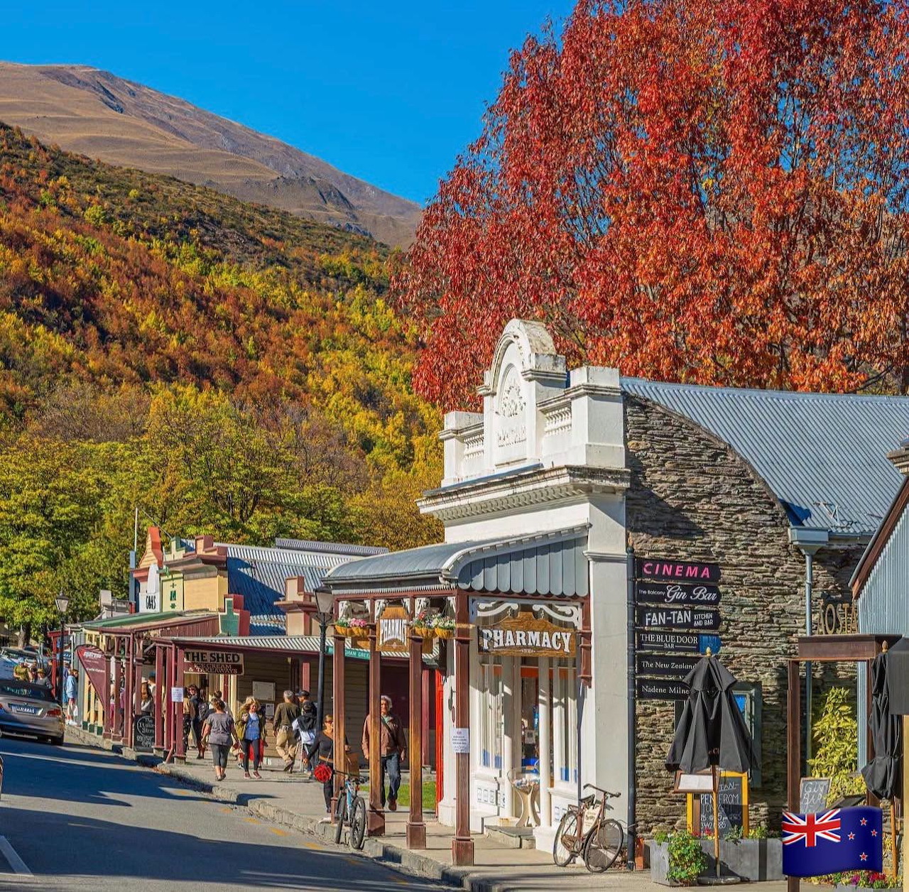 Historic Arrowtown main street with stone buildings and bright red autumn trees against green hills