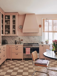 Pink kitchen with marble backsplash, checkered floor, pink cabinets, and stainless steel oven