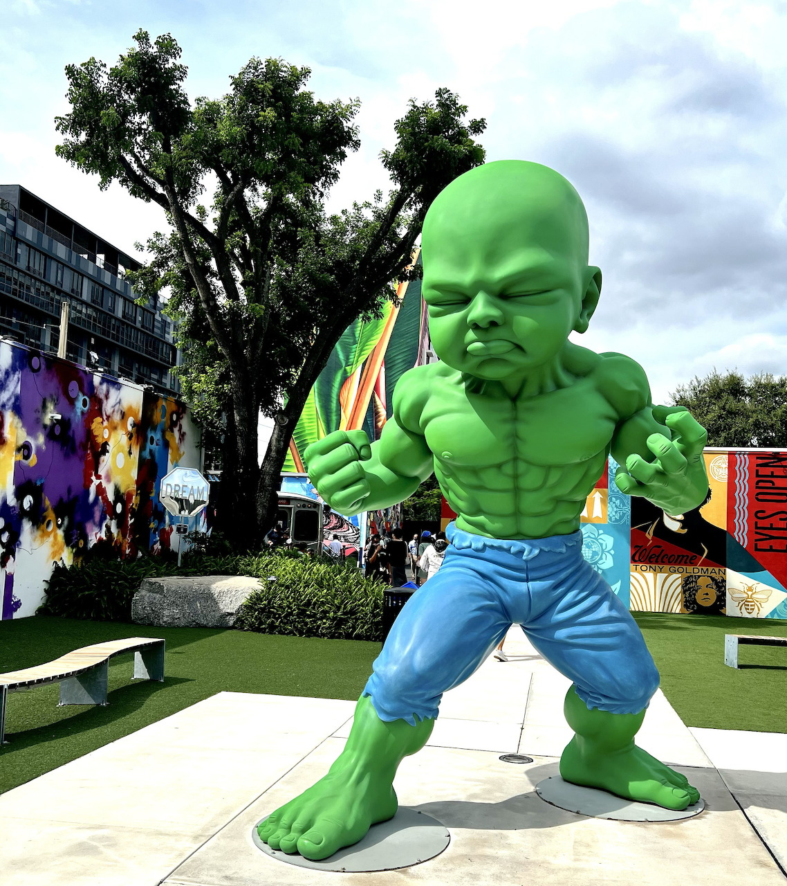 Green muscular cartoon-style baby sculpture in fighting stance in an outdoor park