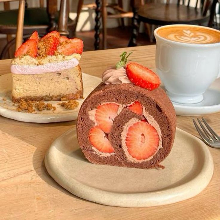Chocolate strawberry Swiss roll cake on a plate with a latte and another strawberry cake slice