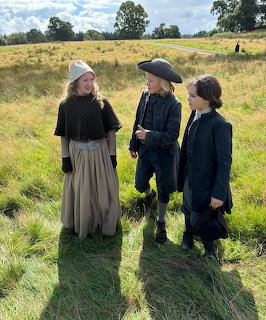 Three people in historical clothing standing in a grassy field outdoors