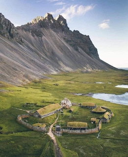 Aerial view of turf-roofed farm buildings in a green valley below rocky mountain peaks
