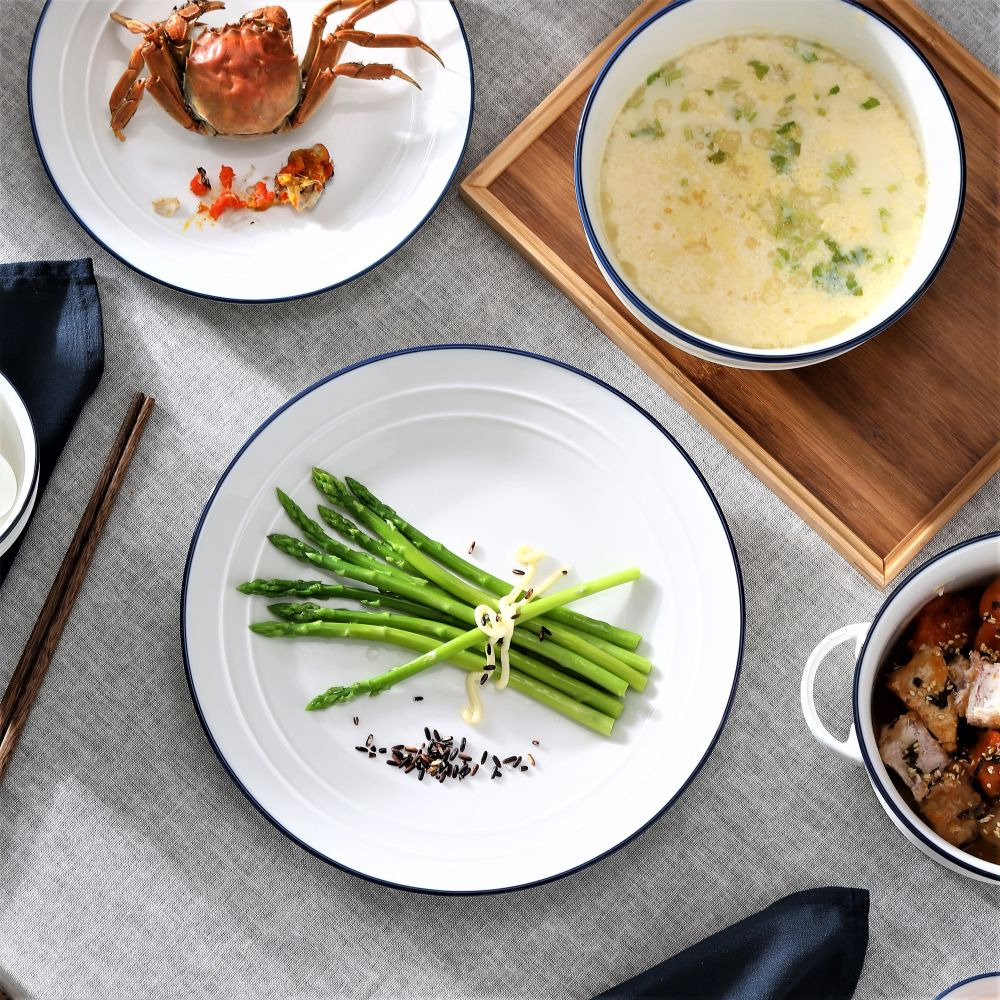 Overhead view of asparagus on a white plate with creamy soup, crab shell, and side dish on a table