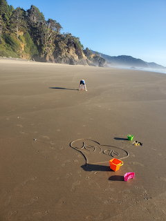 Person walking on expansive sandy beach with coastal cliffs and toys scattered in foreground
