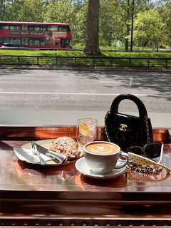 Coffee and pastries on a wooden table by a window with a street and park outside