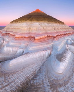 Colorful layered hill above pale eroded badlands under a pink and blue sky