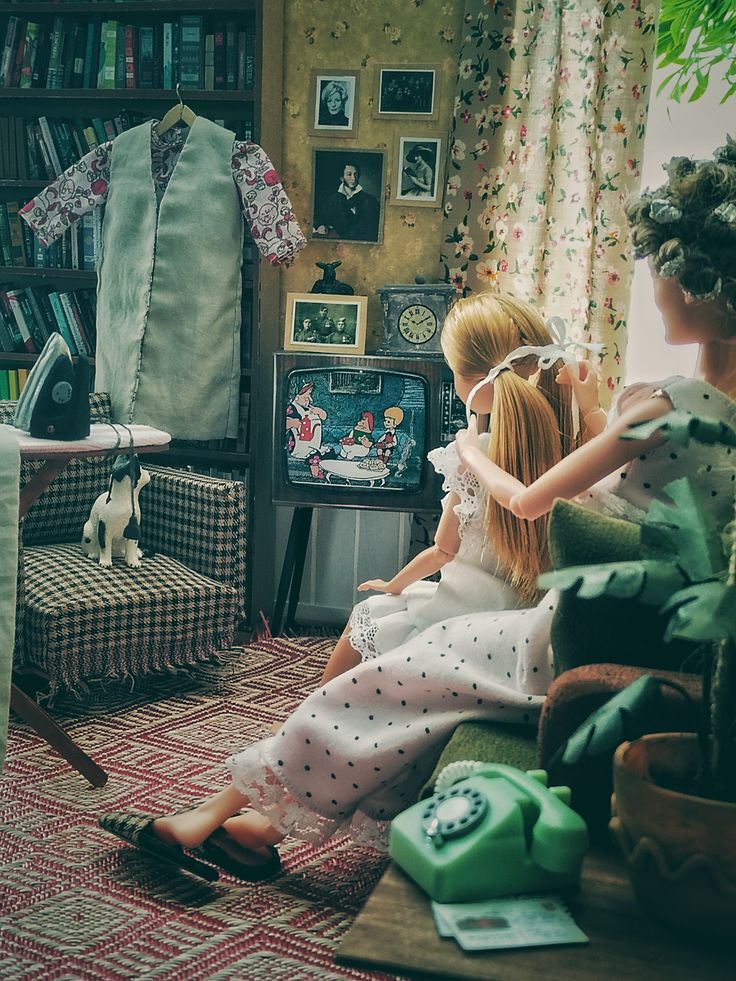 Two Barbie dolls in a vintage miniature living room watching a retro TV with classic decor