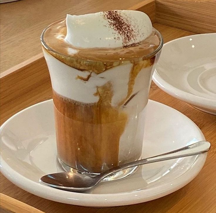Glass of layered Einspänner coffee with whipped cream on a white saucer and spoon