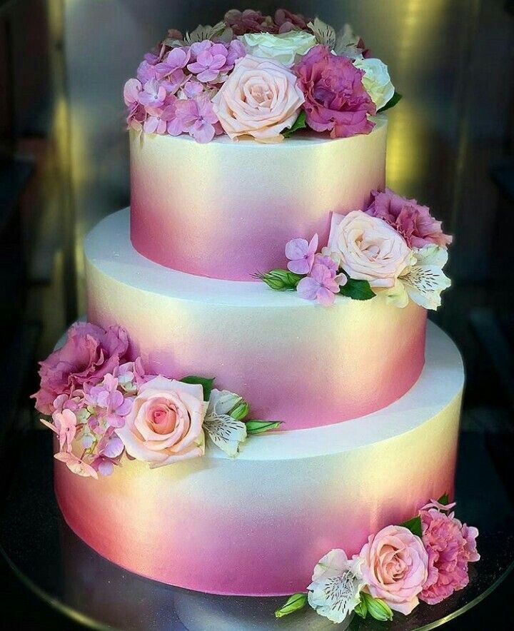 Three-tier pink ombre cake with roses and pink floral decorations